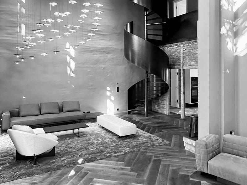 Zweigeschossige Wohnhalle mit Sofas, Fischgrätparkett, Wendeltreppe und Leuchteninstallation, schwarzweiß