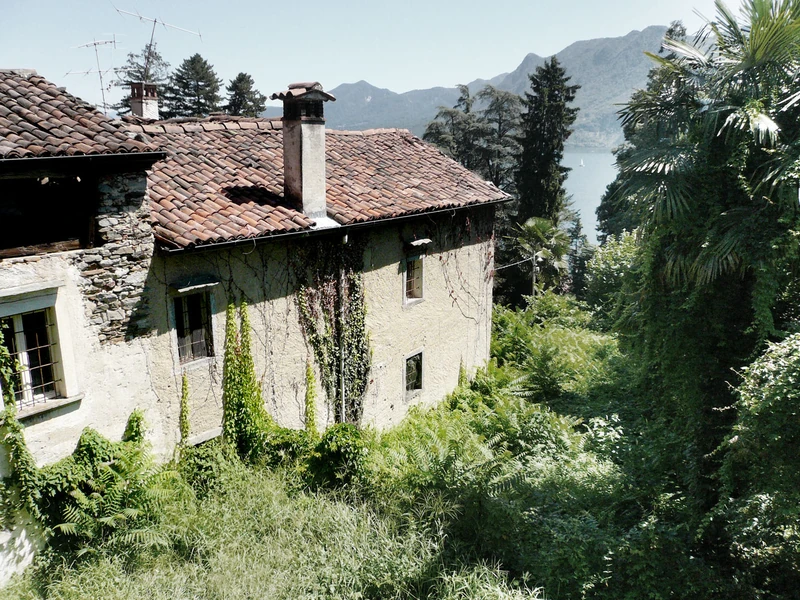 Rustico aus Naturstein mit Ziegeldach und dichtem Bewuchs vor dem Umbau