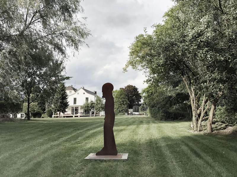 Weitläufige Rasenfläche mit Skulptur und dem Haus im Hintergrund