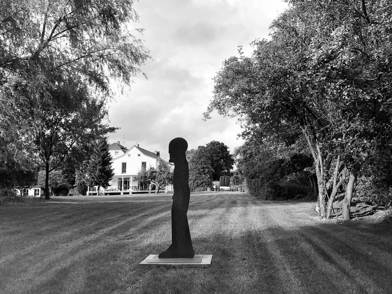Weitläufiger Garten mit Skulptur, im Hintergrund das Haus, schwarzweiß