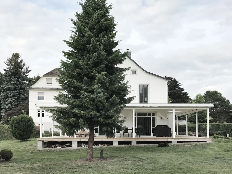 Landhaus mit Veranda hinter einer großen Tanne