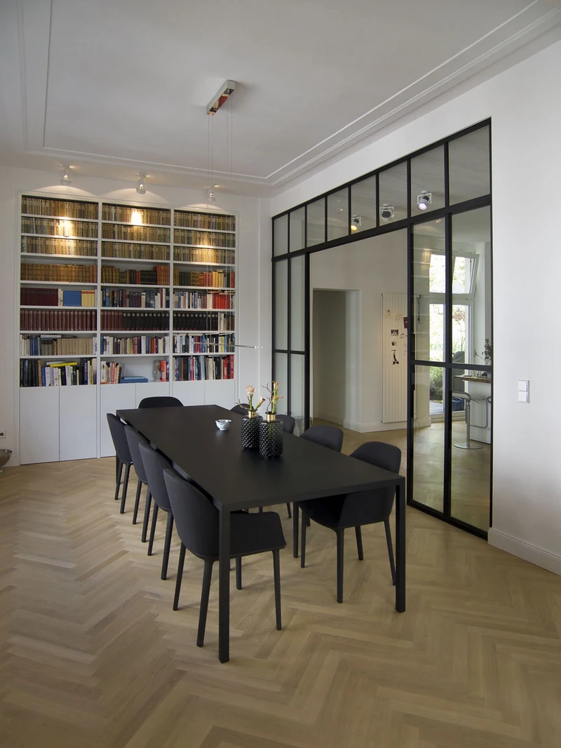 Essbereich mit langem Tisch vor beleuchteter Bücherwand und Stahl-Glas-Trennwand
