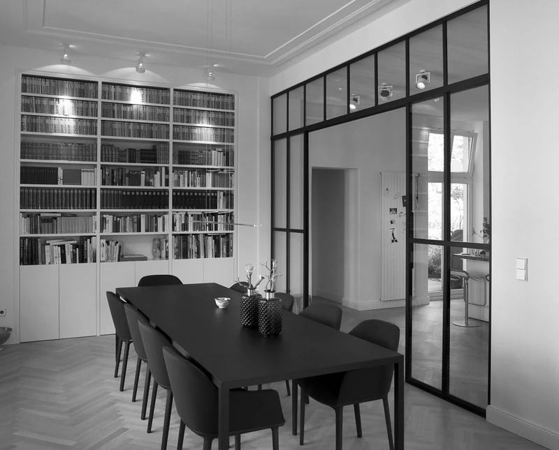 Essbereich mit langem Tisch, Bücherwand und Glastrennwand mit Stahlrahmen, schwarzweiß