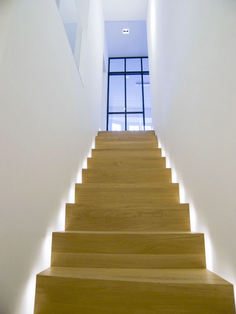 Holztreppe mit indirektem Lichtband zwischen weißen Wänden