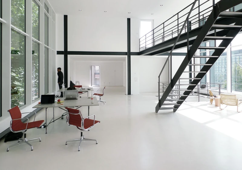 Lichtdurchflutete Halle mit Stahltreppe, Galerie und roten Bürostühlen