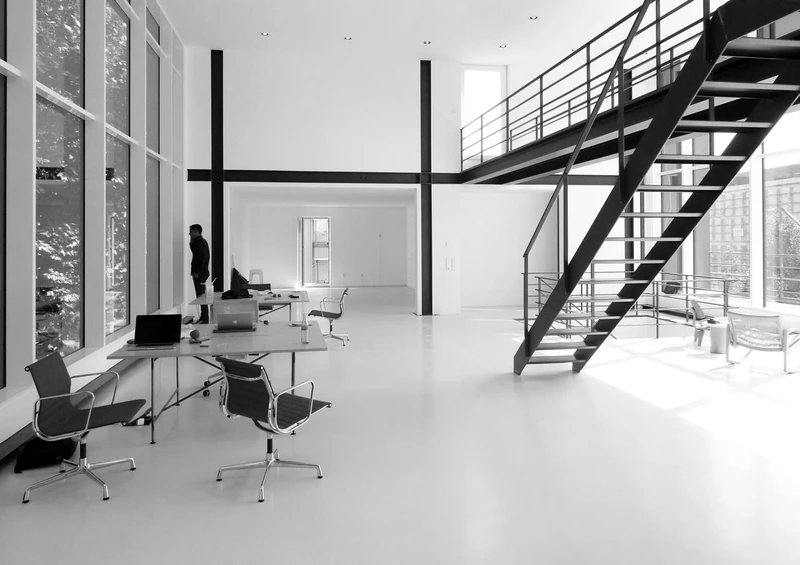 Zweigeschossige Halle mit Stahltreppe, Galerie und Arbeitsplätzen, schwarzweiß